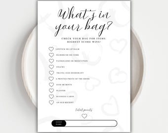 May include: A white card with the text "What's in your bag?" in elegant script. The card includes a checklist of items like lipstick, snacks, and business cards, designed for a bridal shower game. The card is placed on a white plate.