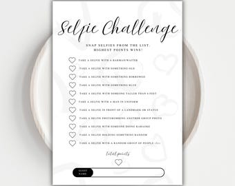 May include: A white paper game card titled "Selfie Challenge" with a list of selfie prompts. The card features a cursive title and a series of heart-shaped bullet points. The bottom includes a space for the guest's name and total points.