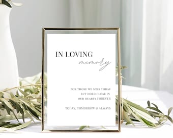 Puede incluir: Un cartel con marco dorado con el texto "IN LOVING memory" y un mensaje sobre recordar a los que se echan de menos. El cartel está sobre una superficie blanca con follaje verde.