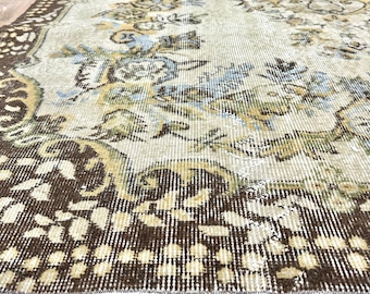 May include: A vintage rug with a cream background and a brown floral pattern. The rug has a distressed look and a white fringe border.