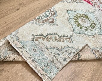 May include: A folded vintage rug with a cream background and intricate floral patterns in shades of blue, green, and brown.