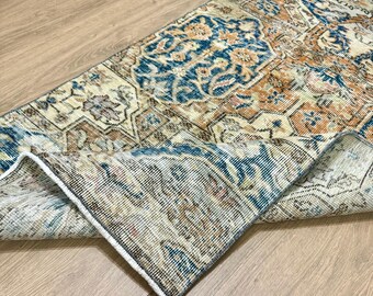 May include: A vintage rug with a cream background and intricate blue and orange floral patterns. The rug is folded in half, showing the texture and detail of the weave.