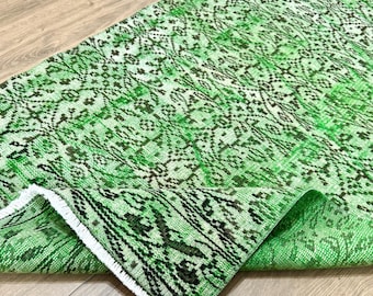 May include: A green and black patterned rug with a distressed, vintage appearance. The rug has a detailed floral design and a fringed edge. The colour scheme includes shades of green and black, creating a unique aesthetic.