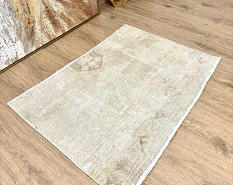 May include: A light beige area rug with a distressed, vintage look. The rug has a white fringe border and is made of a soft, woven material.