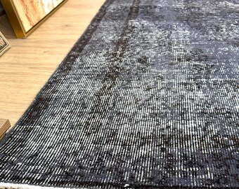 May include: A distressed black and white rug with a rectangular shape. The rug has a faded, vintage appearance with a pattern of vertical lines, creating a textured effect. The edges are finished with a white border. The rug is suitable for a living room.