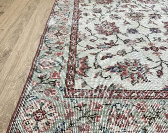 May include: A vintage rug with a floral pattern in shades of red, white, and green. The rug has a fringed edge and is made of a soft, woven material.