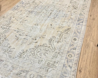 May include: A vintage rug with a faded floral pattern in shades of beige and grey. The rug has a fringed edge and is made of a soft, woven material.