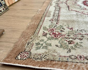 May include: A vintage floral patterned rug with a beige background and a brown border. The rug has a distressed look and is made of a woven material.