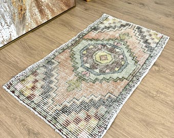 May include: A vintage style rug with a geometric pattern in shades of pink, green, brown, and white. The rug has a fringed edge and is made of wool.