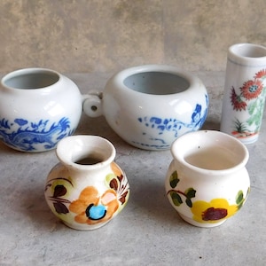 May include: Five small ceramic vases with floral designs. Two of the vases have blue and white floral patterns, one has a yellow and brown floral pattern, one has a yellow and orange floral pattern, and one has a white and green floral pattern.