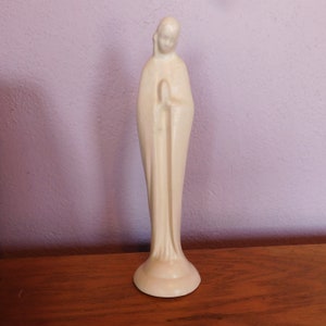 May include: A white ceramic statue of a woman in a long robe with her hands clasped in prayer.