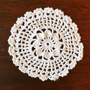 May include: White crocheted doily with a delicate floral design in the center.