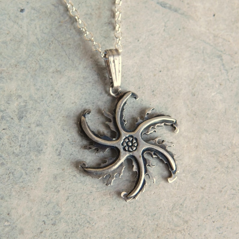 Op de afbeelding: Zilveren ketting met een gedetailleerde stervormige hanger. De hanger heeft een centraal bloemmotief en ingewikkelde, puntige randen.
