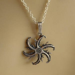 Op de afbeelding: Een zilveren ketting met een stervormige hanger. De hanger heeft een gedetailleerd ontwerp met een kleine bloem in het midden.