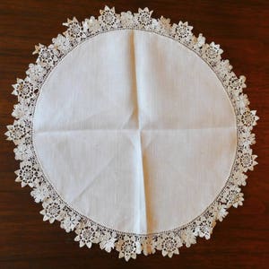 May include: A white crocheted doily with a delicate floral pattern. The doily is round and has a scalloped edge.