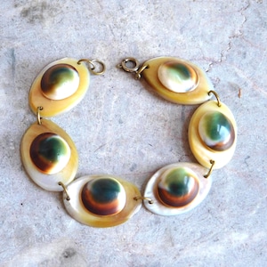 May include: A bracelet composed of five oval-shaped shell links connected by small metal jump rings. Each link features a smooth, polished, dome-shaped center with a gradient of white, green, and brown tones, set against a pale yellow shell base.