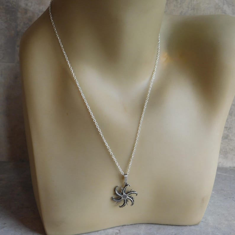 Op de afbeelding: Een zilveren ketting met een zilveren hanger in de vorm van een gestileerde ster met meerdere punten.