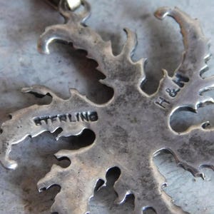 Op de afbeelding: Een zilveren hanger in de vorm van een boom met ingewikkelde details. De achterkant van de hanger is gestempeld met "STERLING" en "H&H".
