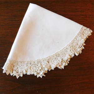 May include: A white cotton tablecloth with a delicate lace trim. The lace is a cream color and has a floral pattern.