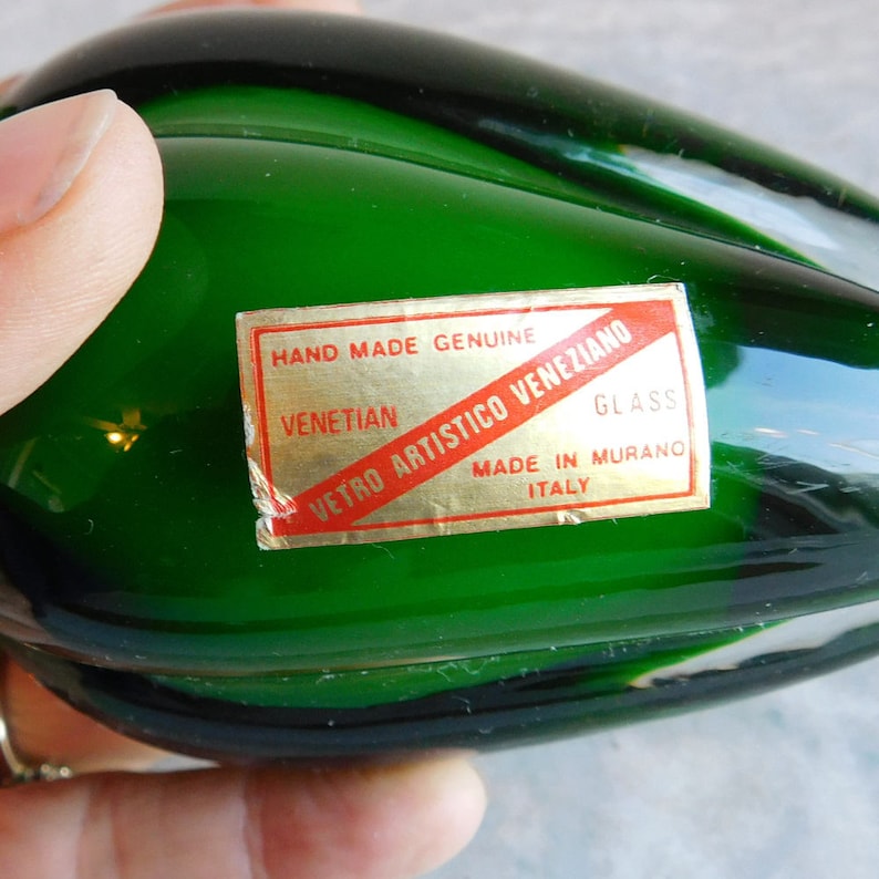 May include: A green glass paperweight with a label that reads "Hand Made Genuine Venetian Vetro Artistico Veneziano Glass Made in Murano Italy".