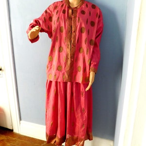 May include: A pink and gold two-piece outfit with a long-sleeved button-up top and a skirt. The top and skirt have a repeating pattern of gold circles on a pink background.