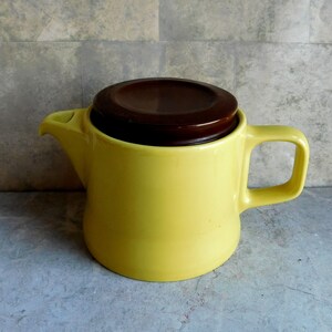May include: A yellow ceramic teapot with a brown lid. The teapot has a handle and a spout.
