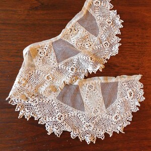 May include: Two delicate white lace collars with a scalloped edge. The collars are made of a fine mesh fabric with intricate crochet details.