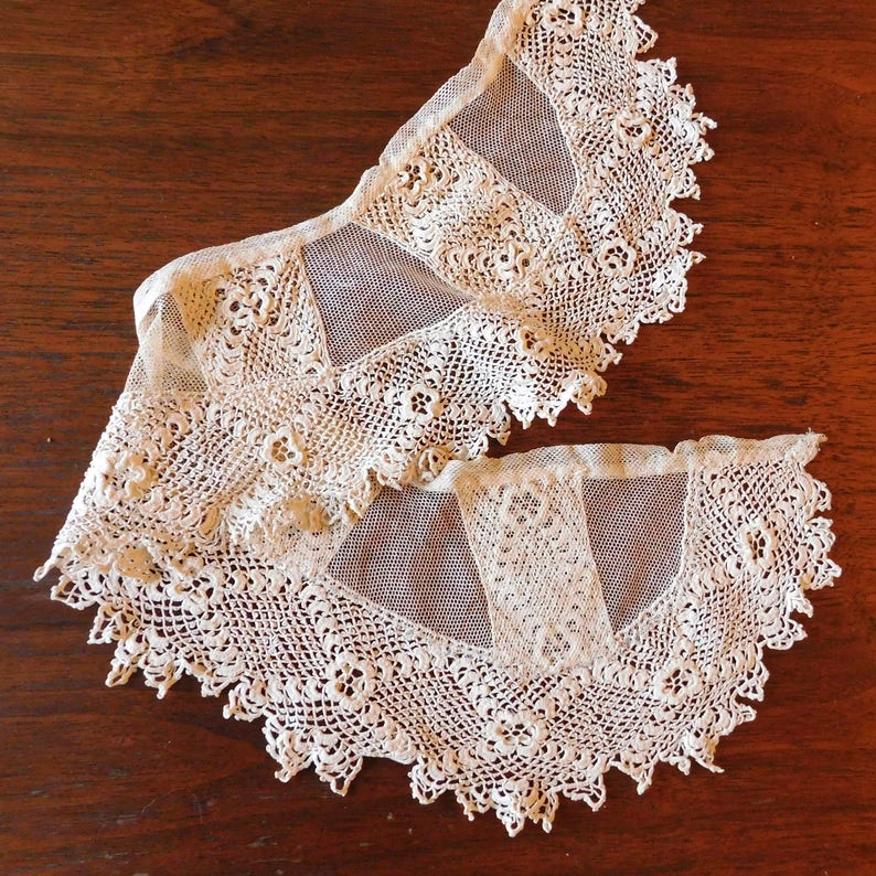 May include: Two delicate white lace collars with a scalloped edge. The collars are made of a fine mesh fabric with intricate crochet details.