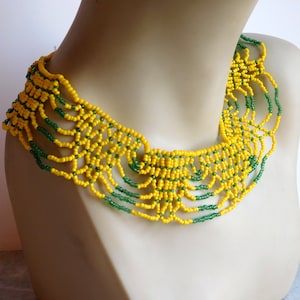 Pode incluir: Um colar de contas amarelas e verdes com um design em camadas. O colar é feito de contas pequenas e redondas e tem uma forma festoneada.