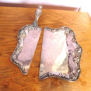 Puede incluir: Juego de servidor de pastel plateado y plato a juego. El servidor tiene un mango decorativo y una hoja con borde curvo. Ambas piezas están adornadas con diseños de uvas y hojas a lo largo de los bordes, creando una estética vintage elegante.