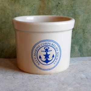 Könnte beinhalten: Weiße Keramik-Kanne mit einem blau-weißen Logo der Navy-Marine Corps Relief Society. Das Logo zeigt einen Anker und einen Stern.