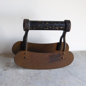 May include: An antique, hand-held food chopper with a black handle and two curved, brown blades. The blades are connected to the handle by metal supports. The chopper is made of metal and shows signs of wear.
