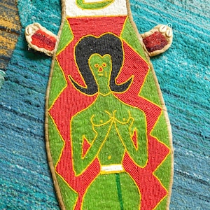 May include: A beaded wall hanging with a green figure with black hair and red and yellow accents.