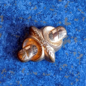 May include: A gold-toned metal brooch with a knot design and intricate floral details.