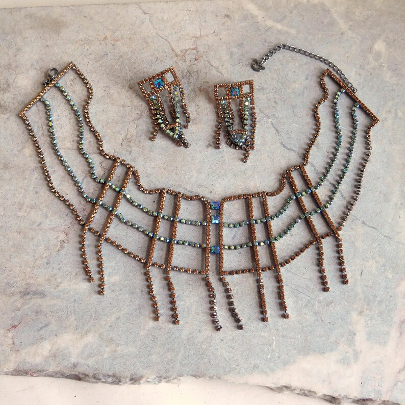 May include: A brown and blue rhinestone necklace with a geometric design and dangling fringe. The necklace is paired with matching earrings.