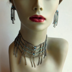 May include: A silver choker necklace with a geometric design and dangling blue crystal accents.
