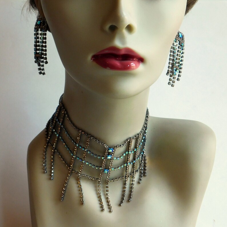 May include: A silver choker necklace with a geometric design and dangling blue crystal accents.