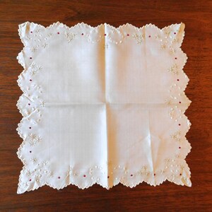 May include: A white cotton handkerchief with a scalloped edge and delicate embroidery in red and white.