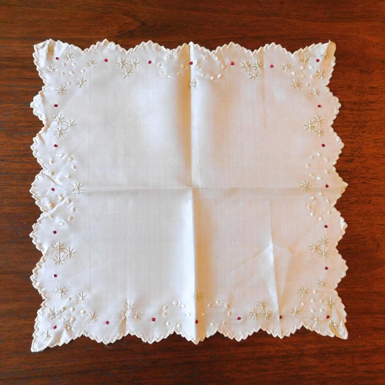 May include: A white cotton handkerchief with a scalloped edge and delicate embroidery in red and white.