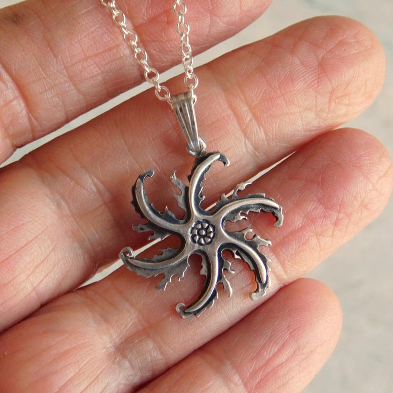 Op de afbeelding: Een zilveren ketting met een gedetailleerde, stervormige hanger. De hanger heeft een getextureerd, bijna stekelig ontwerp.