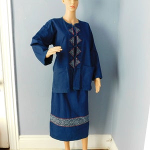 May include: A dark blue, long-sleeved, button-up top with a geometric pattern and a matching skirt. The top has a mandarin collar and two pockets. The skirt has a band of embroidery around the hem.