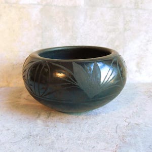 May include: A dark, round ceramic bowl with etched leaf and geometric designs. The bowl has a wide opening and a smooth, glossy finish. The decorative bowl is suitable for holding small items or as a decorative accent.