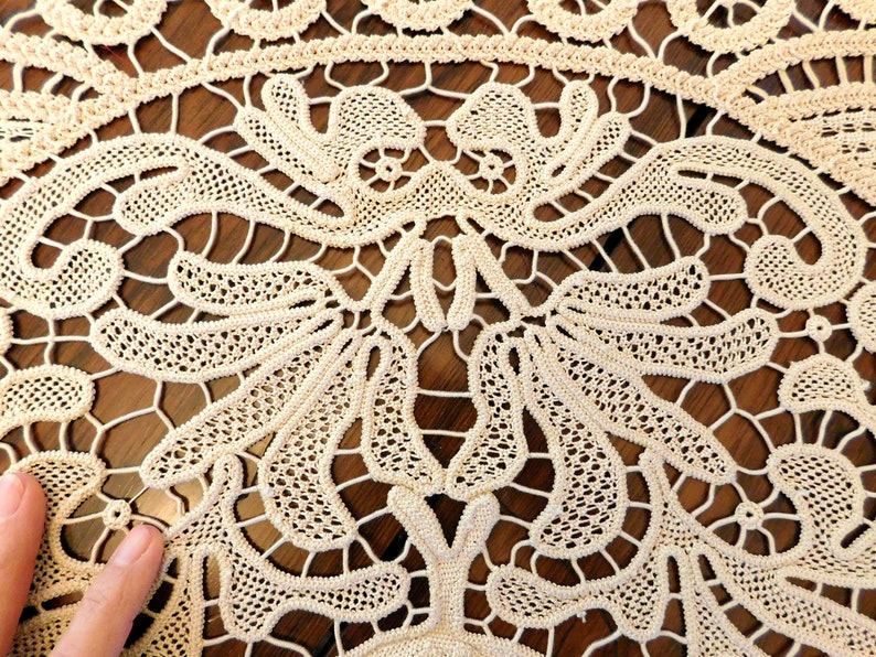 K&ouml;nnte beinhalten: Nahaufnahme einer zarten, cremefarbenen H&auml;keltischdecke mit filigranen Blumenmustern. Die Spitze ist in einem feinen, komplizierten Design gewebt, das einen zarten und eleganten Look erzeugt.