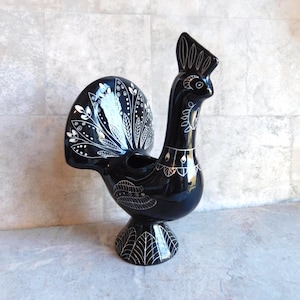 May include: A black ceramic rooster figurine with white decorative accents. The rooster has a detailed tail, crest, and body patterns. The figurine is standing on a pedestal base, showcasing a glossy finish.