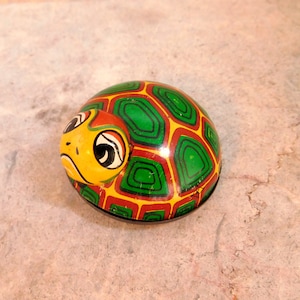 May include: A vintage wind-up toy turtle with a green, red, and yellow shell. The turtle has large, black eyes and a yellow face.