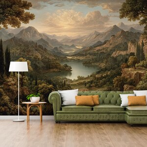 May include: A scenic mural depicting a mountain landscape with a lake, trees, and a sunset. A green sofa with white and orange pillows sits in front of the mural. A white floor lamp and a small table with a plant are also in the room.