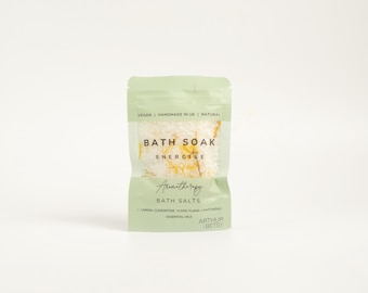 May include: A green pouch with white bath salts and a label that reads "Bath Soak Energise Aromatherapy Bath Salts Lemon, Clementine, Ylang Ylang, Patchouli Essential Oils Arthur Betsy"