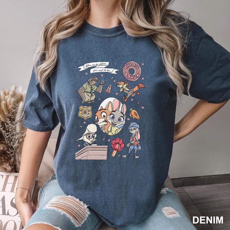 May include: Denim blue t-shirt featuring a colorful cartoon graphic with characters and text from a popular animated movie. The graphic includes the words "THE BIG DONUT" and "You can be whatever you wish to be."