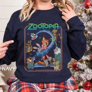 Puede incluir: Sudadera azul marino con un dise&ntilde;o gr&aacute;fico colorido de la pel&iacute;cula animada Zootopia. El dise&ntilde;o incluye el t&iacute;tulo de la pel&iacute;cula y varios personajes, como un zorro, un conejo y un perezoso. La palabra "NAVY" est&aacute; impresa en el lado izquierdo de la sudadera.