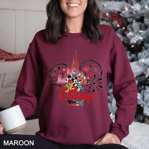 May include: Maroon sweatshirt featuring a Disney design. The graphic includes Disney characters, a castle, fireworks, and the word "Disney" in red. The design is set within Mickey Mouse ear shapes, with the year "2020" below.